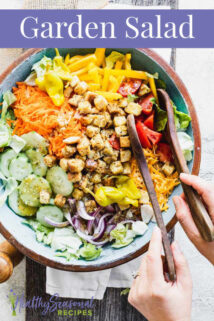 blue bowl with Garden salad in it and a person holding the salad tongs