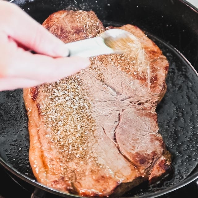 A pan with Steak, sprinkling the spice over it