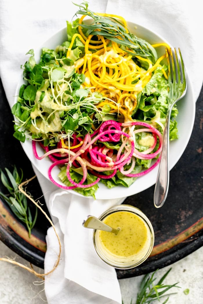 Tarragon vinaigrette in a jar with a big bowl of salad with spiralized veggies