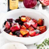 a bowl of beets chunks from the side with a bottle of balsamic vinegar behind it