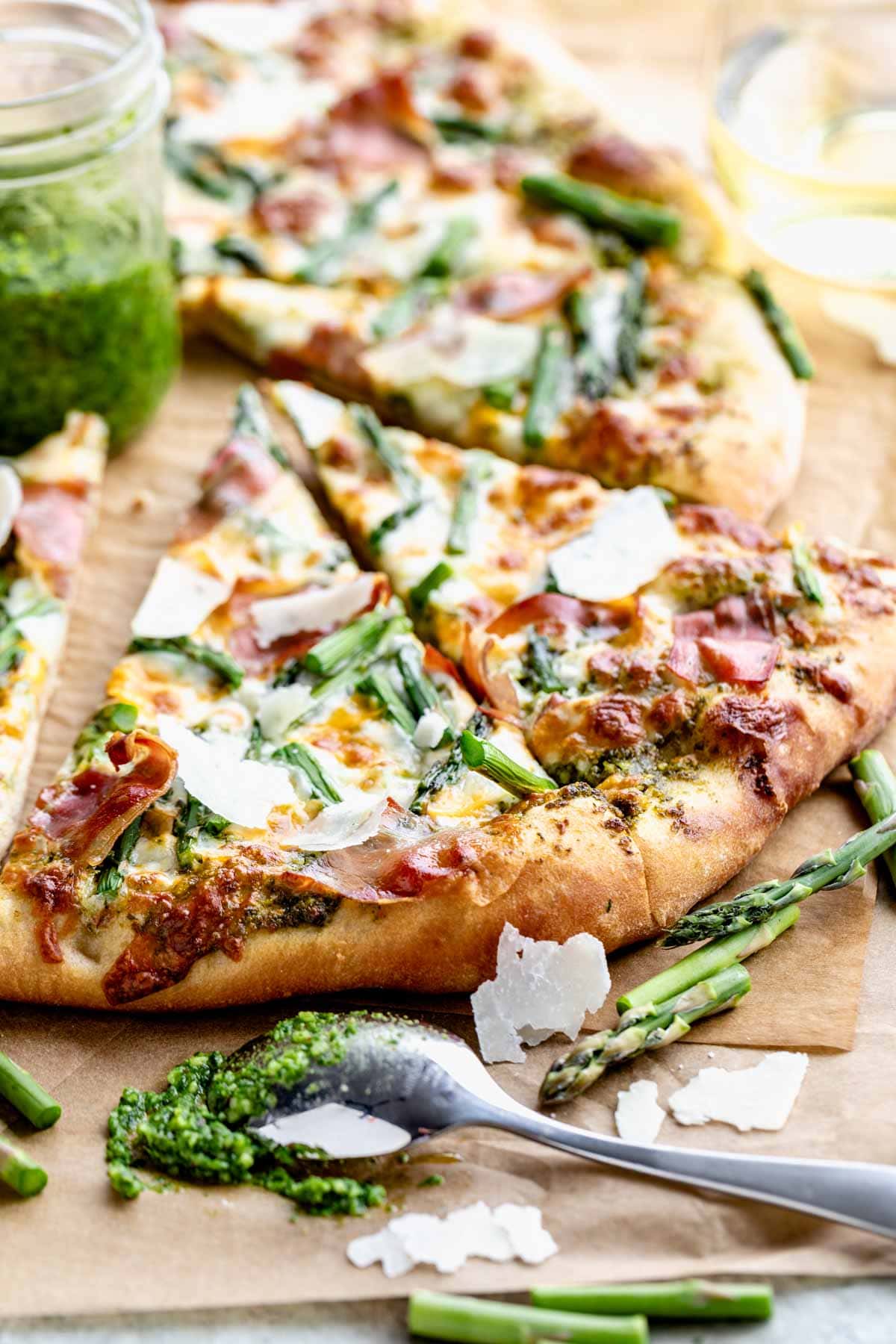 slices of asparagus pizza from the side with a spoon with pesto on it