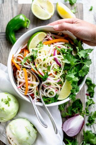 kohlrabi slaw with lime and cilantro in a bowl with a hand holding the bowl