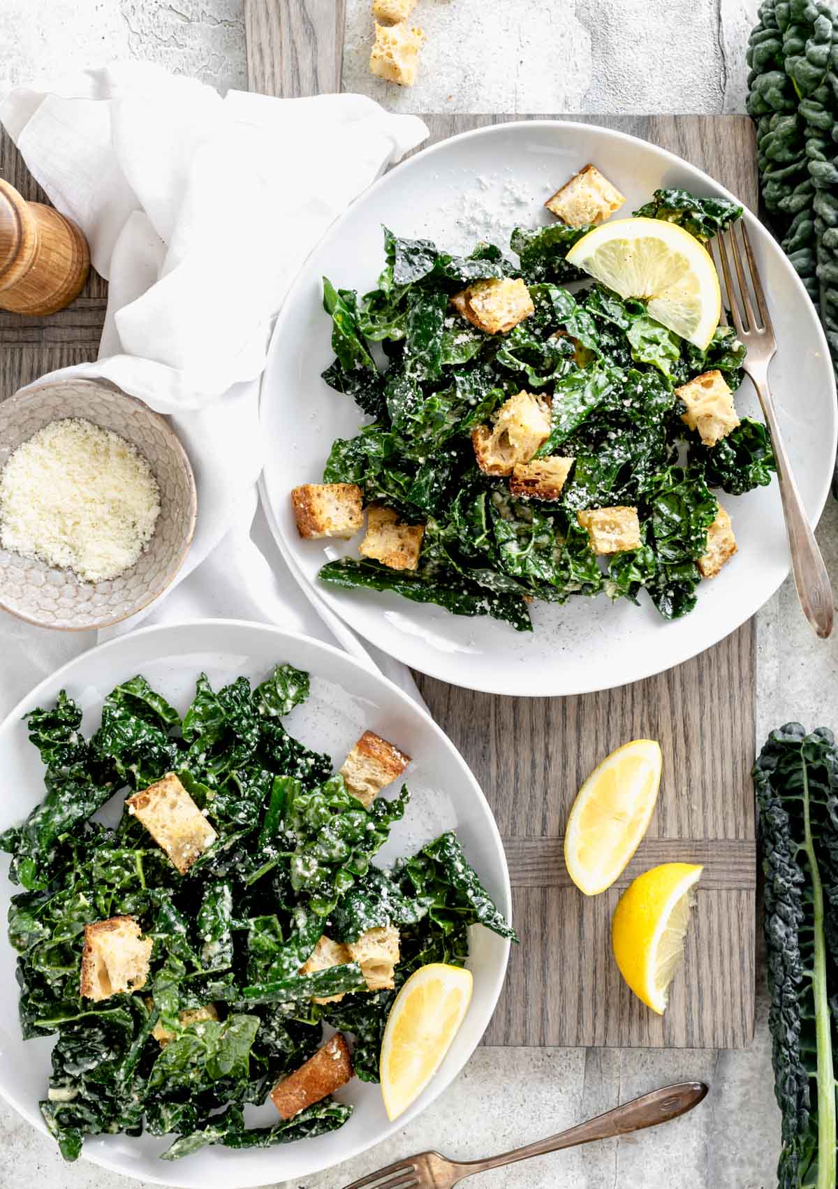 Kale Caesar on two white plates with lemon wedges