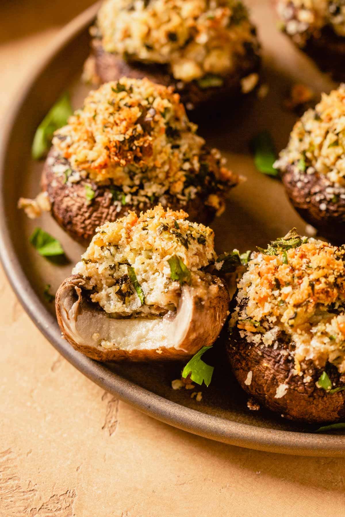 stuffed mushrooms topped with breadcrumbs on a brown plate. One mushroom with a bite taken out of it