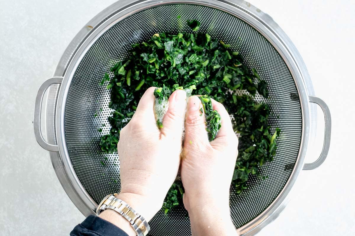 squeezing out excess liquid of frozen spinach into a bowl