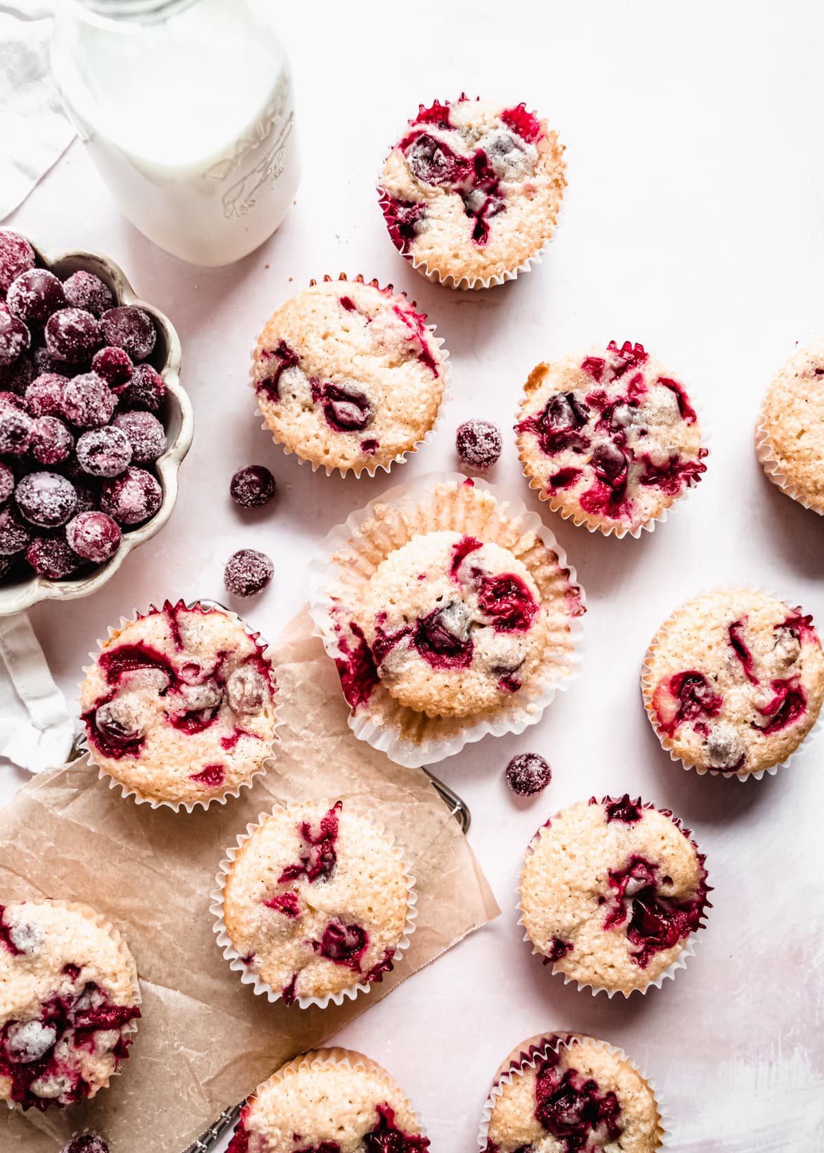 Cranberry orange muffins on parchment paper on counter, sugared cranberries in a bowl 