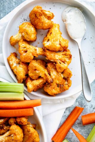 air fryer cauliflower wings on circular white plate with a spoon of creamy dipping sauce