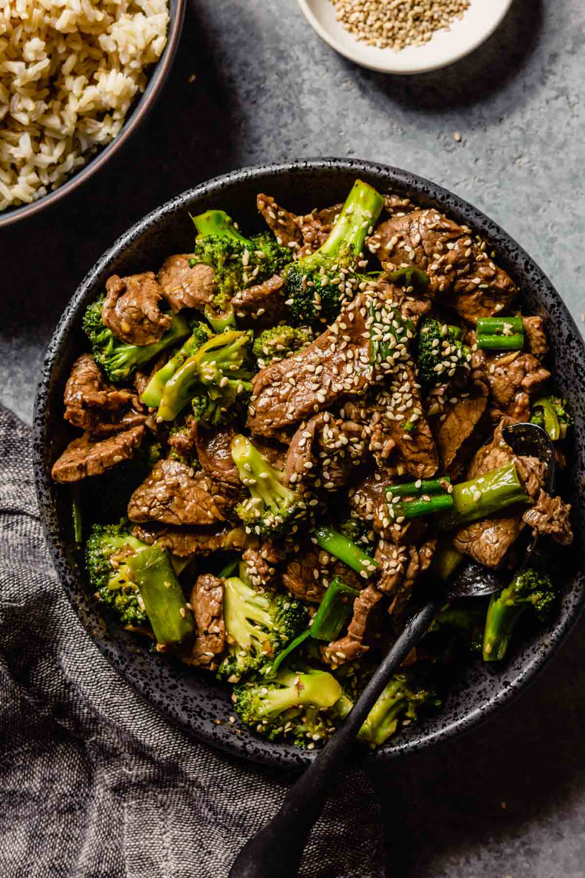 thinly sliced cooked steak and broccoli coated in a sauce and piled into a black bowl