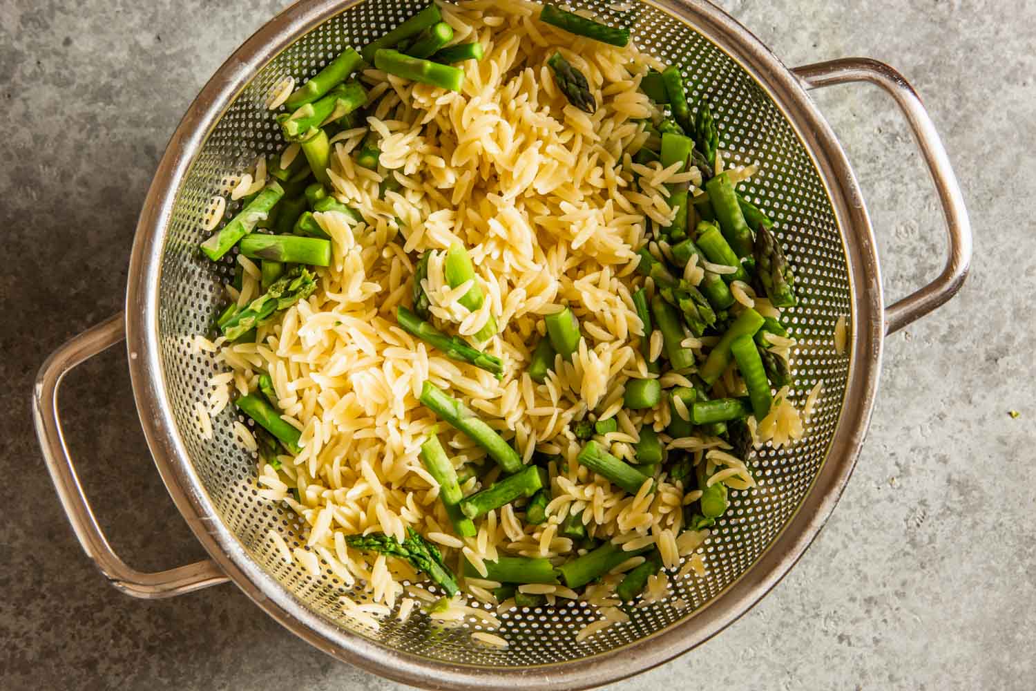 cooked orzo and asparagus in a silver colander