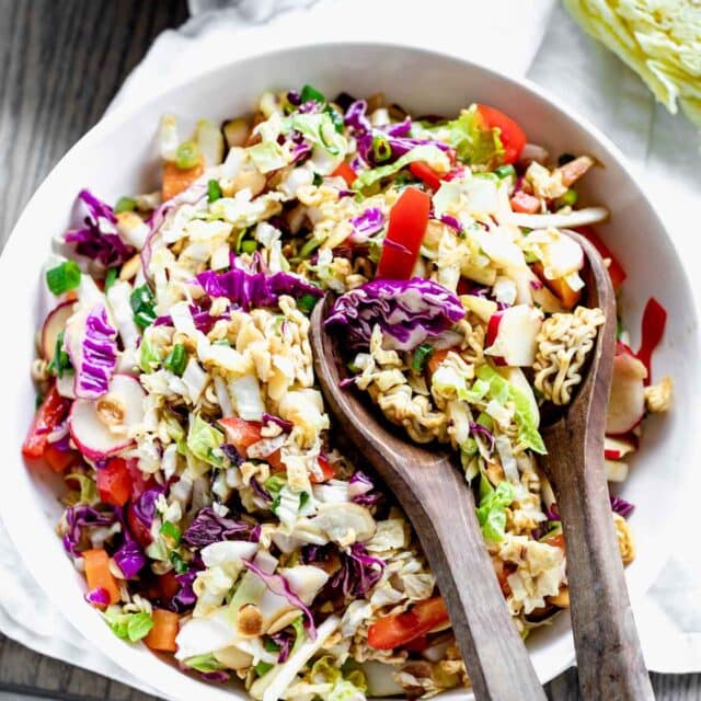 Napa Cabbage Ramen Noodle Salad in a white bowl with wooden salad spoons in it on a table.