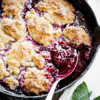 Blackberry cobbler cooked in a black cast iron skillet with a spoon in it.