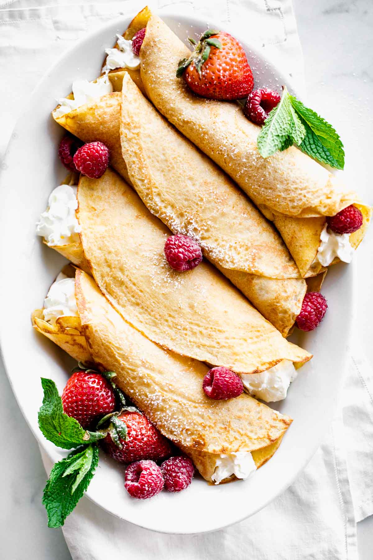 crepes filled with cream and berries on an oval platter