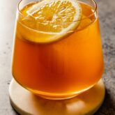 short rocks glass filled with an amber-hued cocktail and lemon wheel