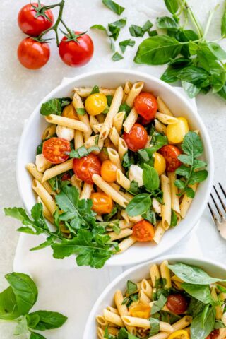 cherry tomato pasta in a white bowl with arugula on a white tabletop