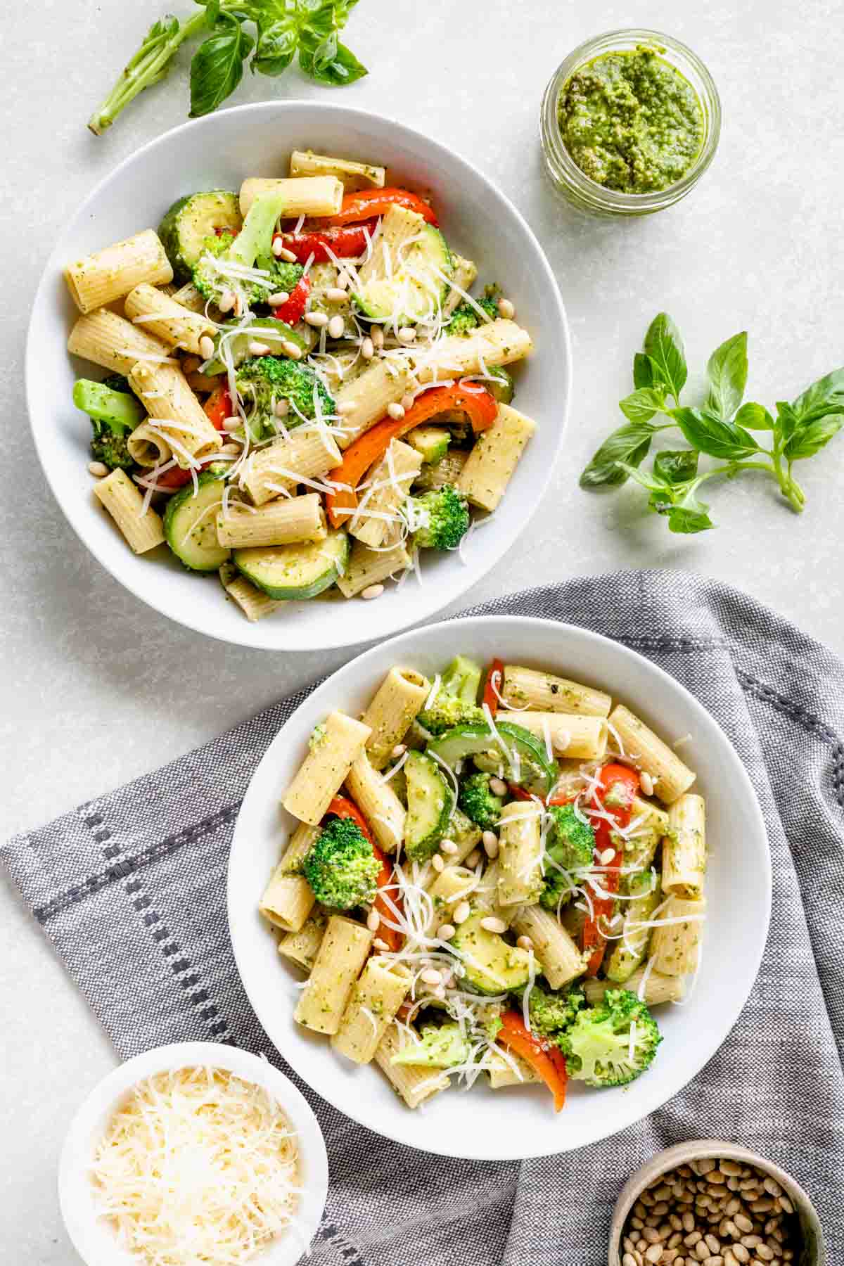two bowls of veggie pesto pasta with pine nuts and parmesan cheese on top
