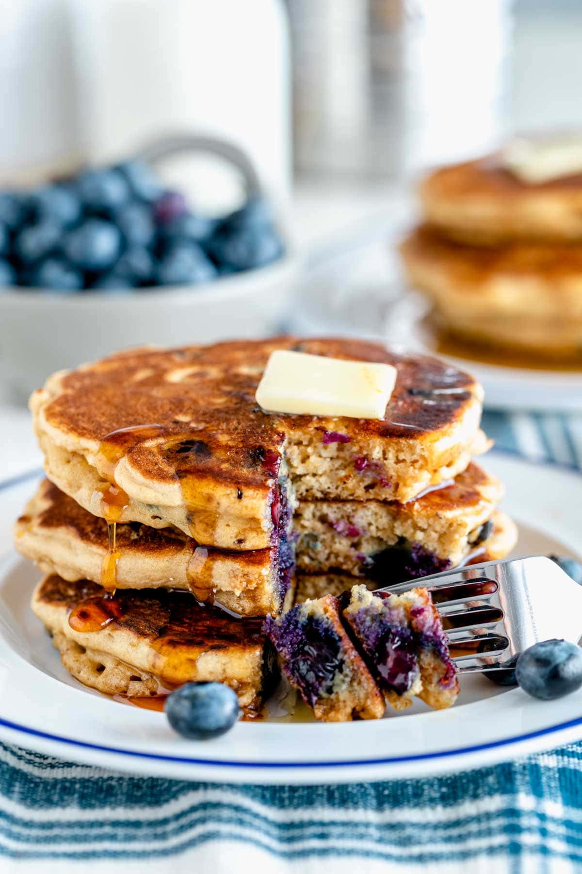 a stack of whole wheat blueberry pancakes with a pat of butter and a bite missing