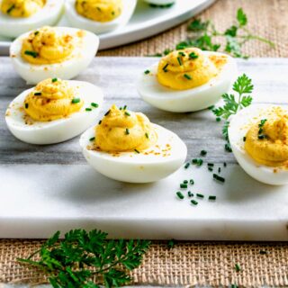 deviled eggs on a white marble board with chives