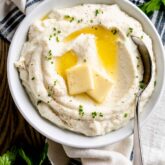 a white bowl with mashed cauliflower topped with melted butter
