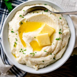 a white bowl with mashed cauliflower in it with melted butter on top and a spoon in it