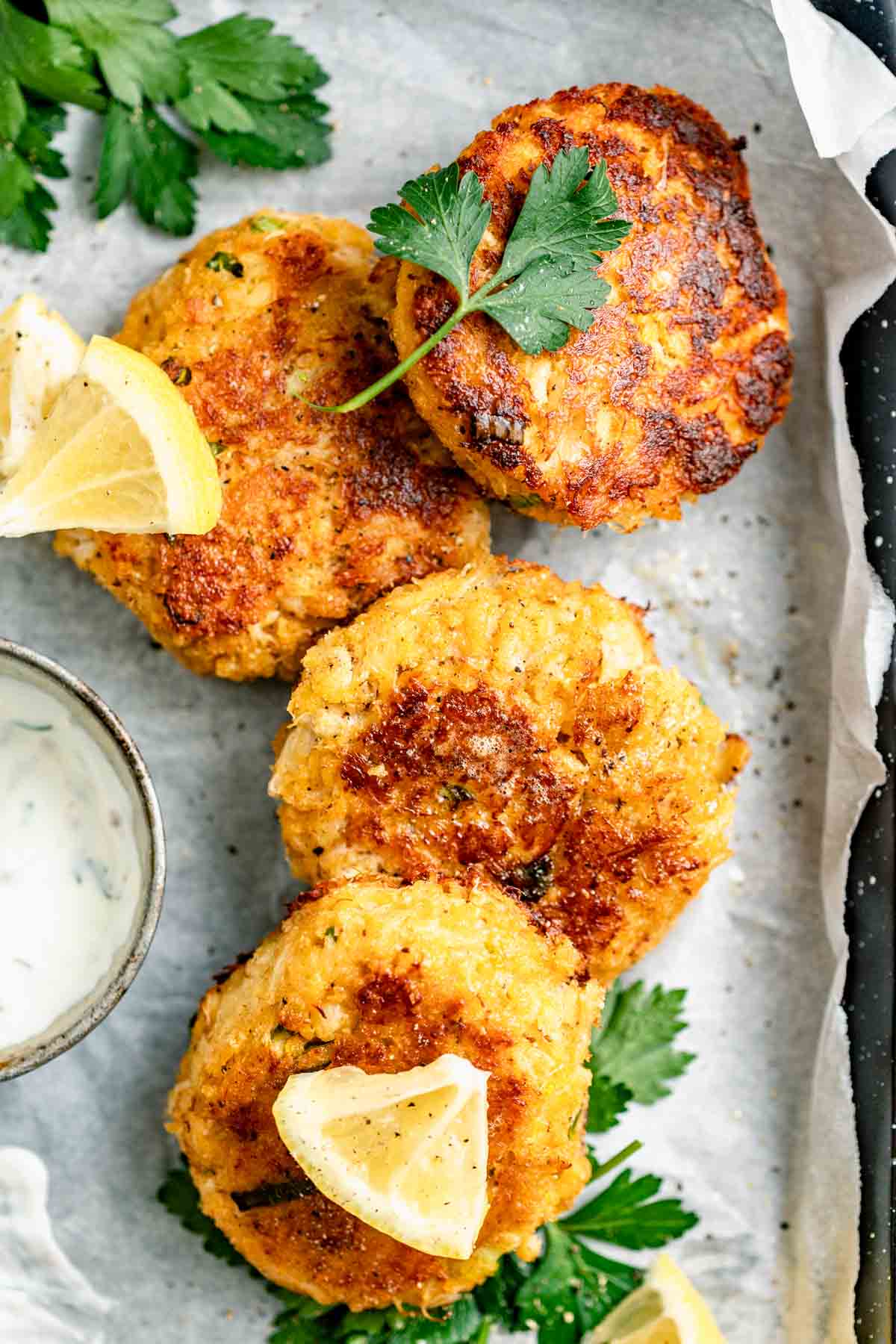 crab cakes on a sheet pan with herbs and lemon slices