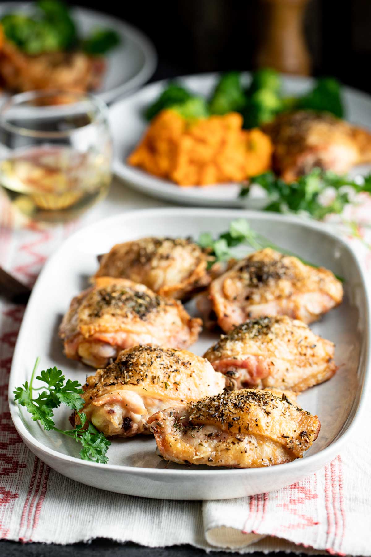 roasted chicken thighs on a platter and a plate of chicken and side dishes in the background