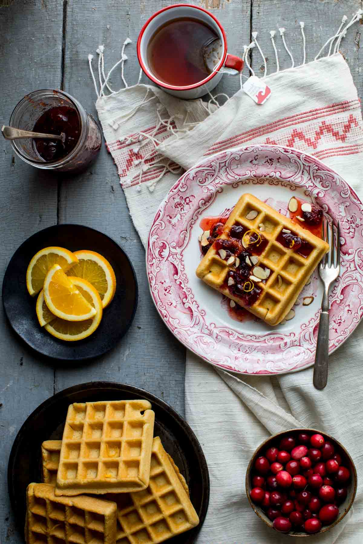 overhead tablescape of the waffles on a platter, then one on a plate topped with cranberry syrup