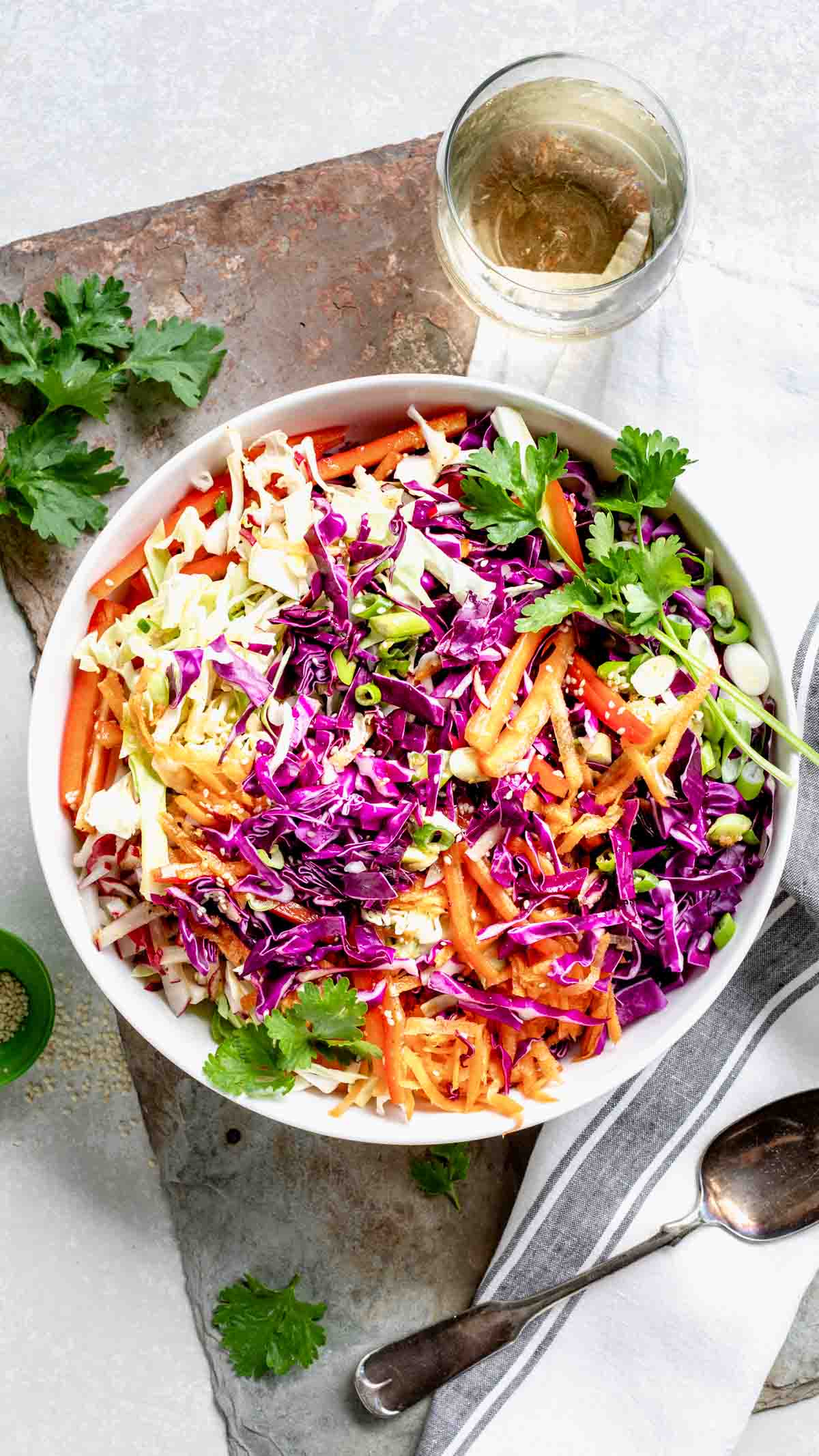 colorful Asian coleslaw in a white bowl on slate board with a glass of white wine