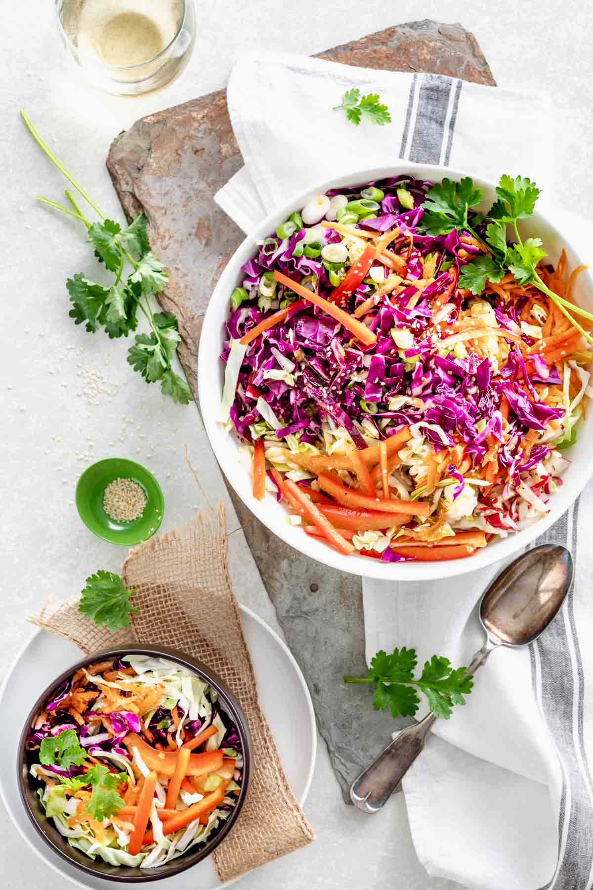 two bowls of the asian coleslaw with a spoon and cilantro leaves