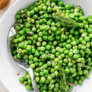 cooked peas in a white bowl with the serving spoon