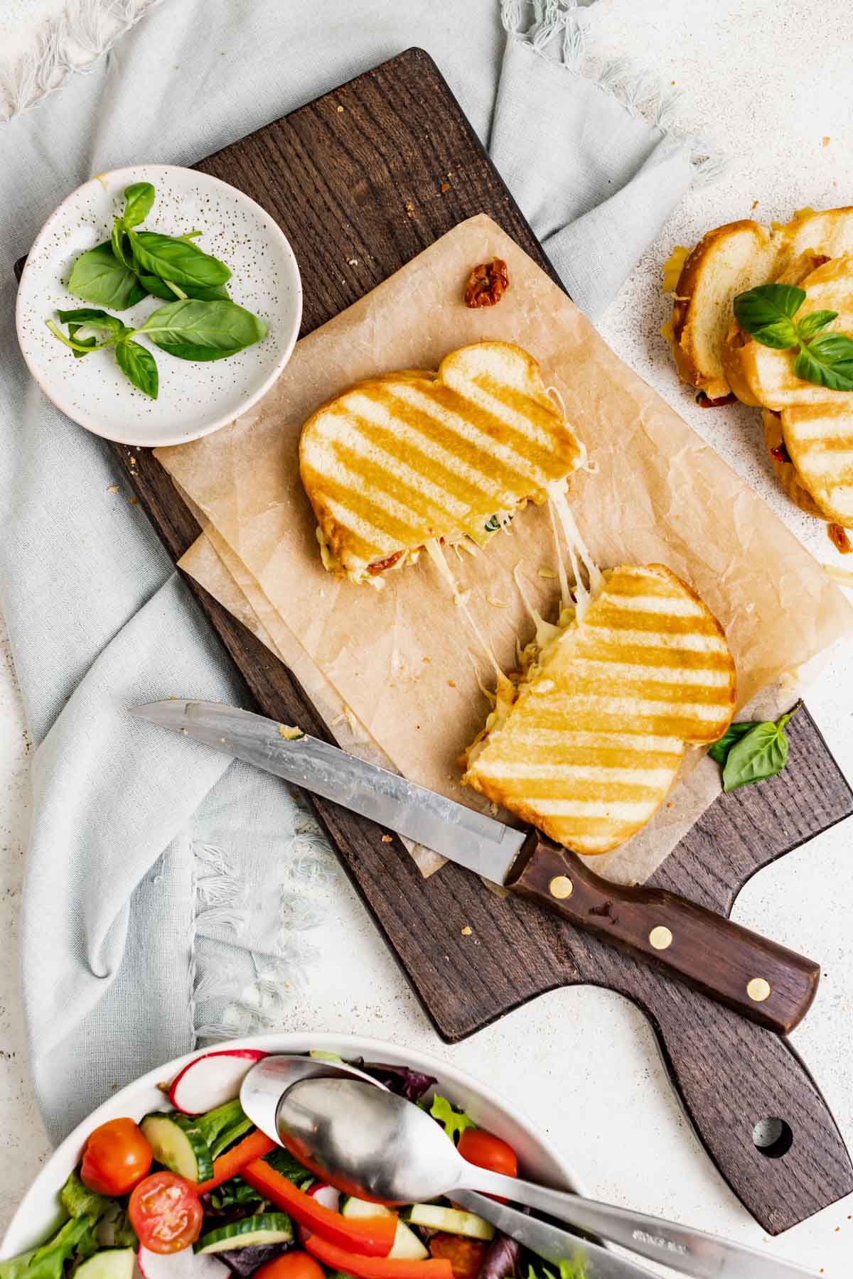 a veggie panini cut in half with cheesy strings pulled between the two pieces while sitting on a parchment-covered cutting board
