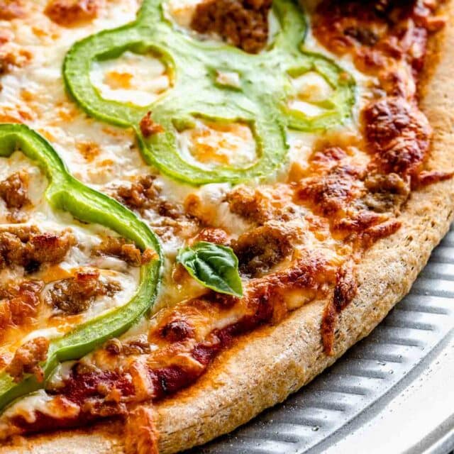 baked homemade whole wheat pizza dough. Close up of the edge of the pizza on a ridged pizza pan.