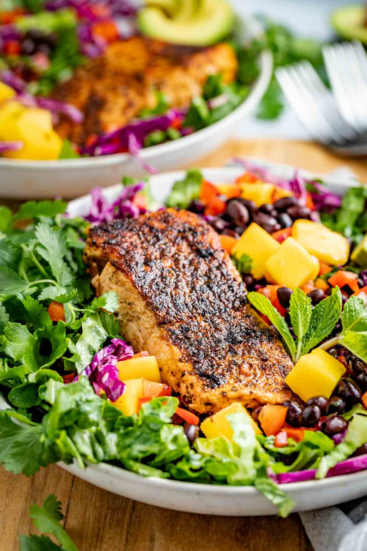 a large bowl of salad with mango, black beans, red cabbage and more, with a filet of blackened salmon on top