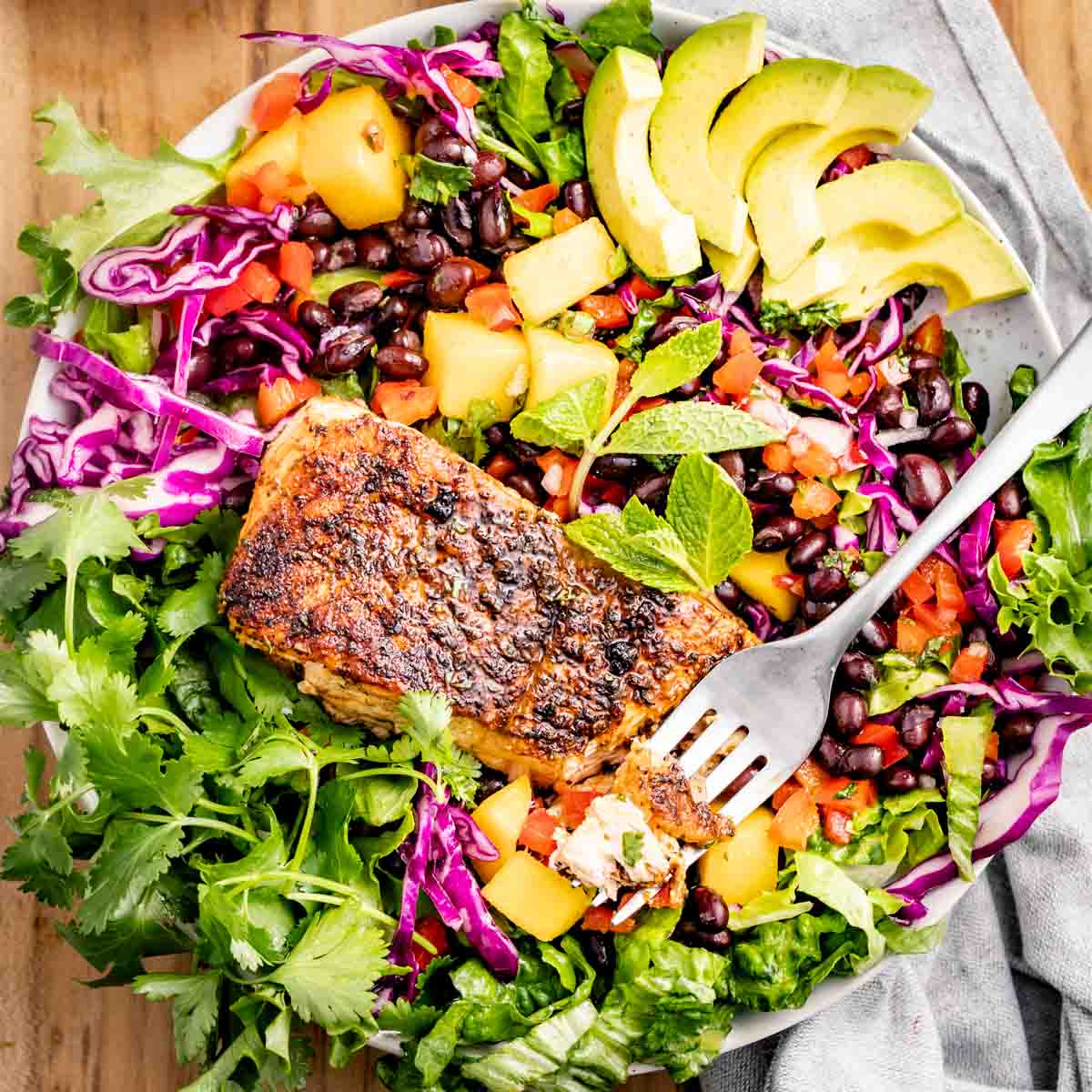 a bowl of salad with mango, black beans, and red cabbage with blackened salmon on top