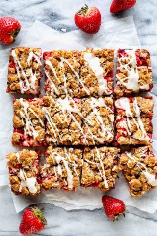 strawberry oatmeal bars drizzled with lemon icing and cut into squares with whole strawberries scattered about