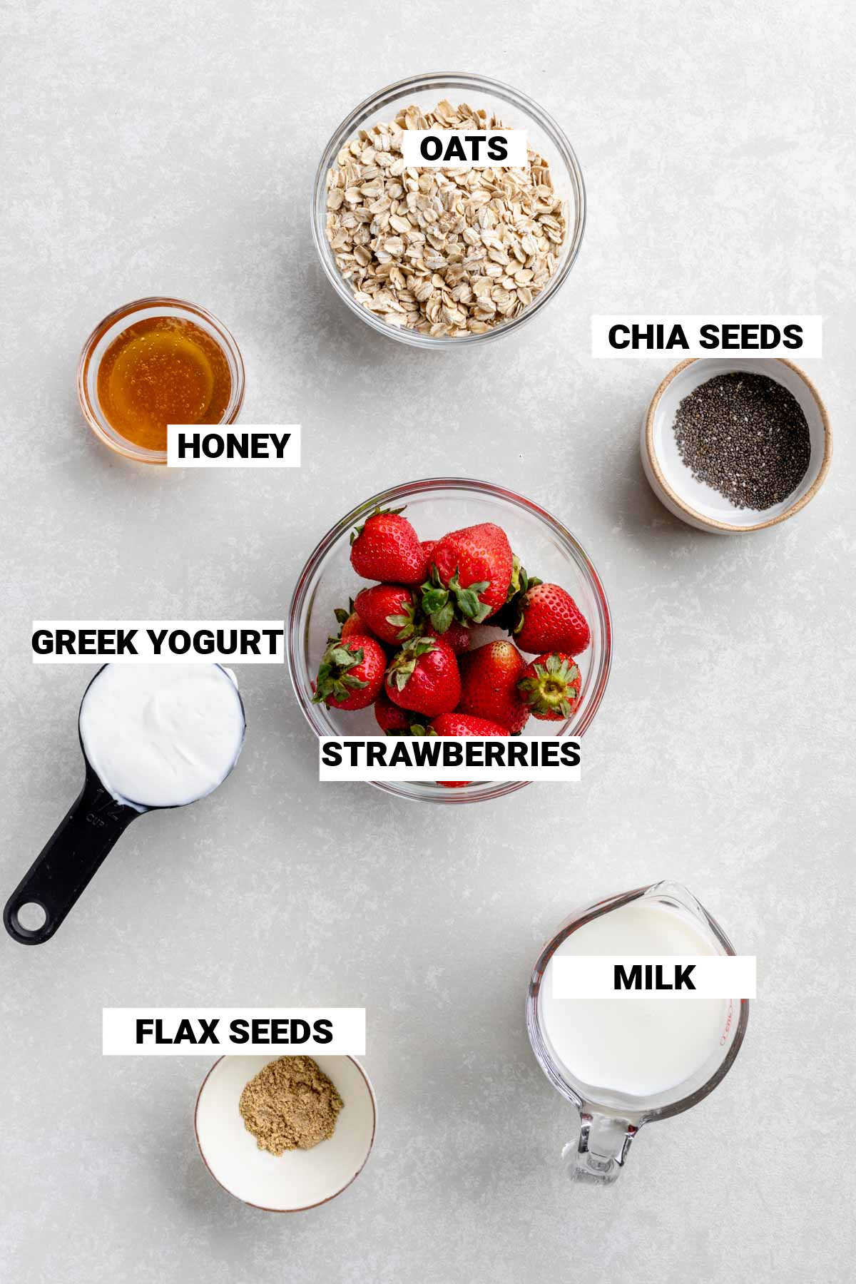 bowls full of oats, chia seeds, honey, greek yogurt, strawberries, milk, and flax seeds to make overnight oats