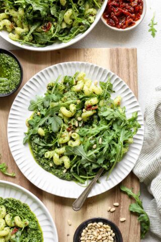 overhead photo of arugula pasta on a circular white plate on a wooden cutting board