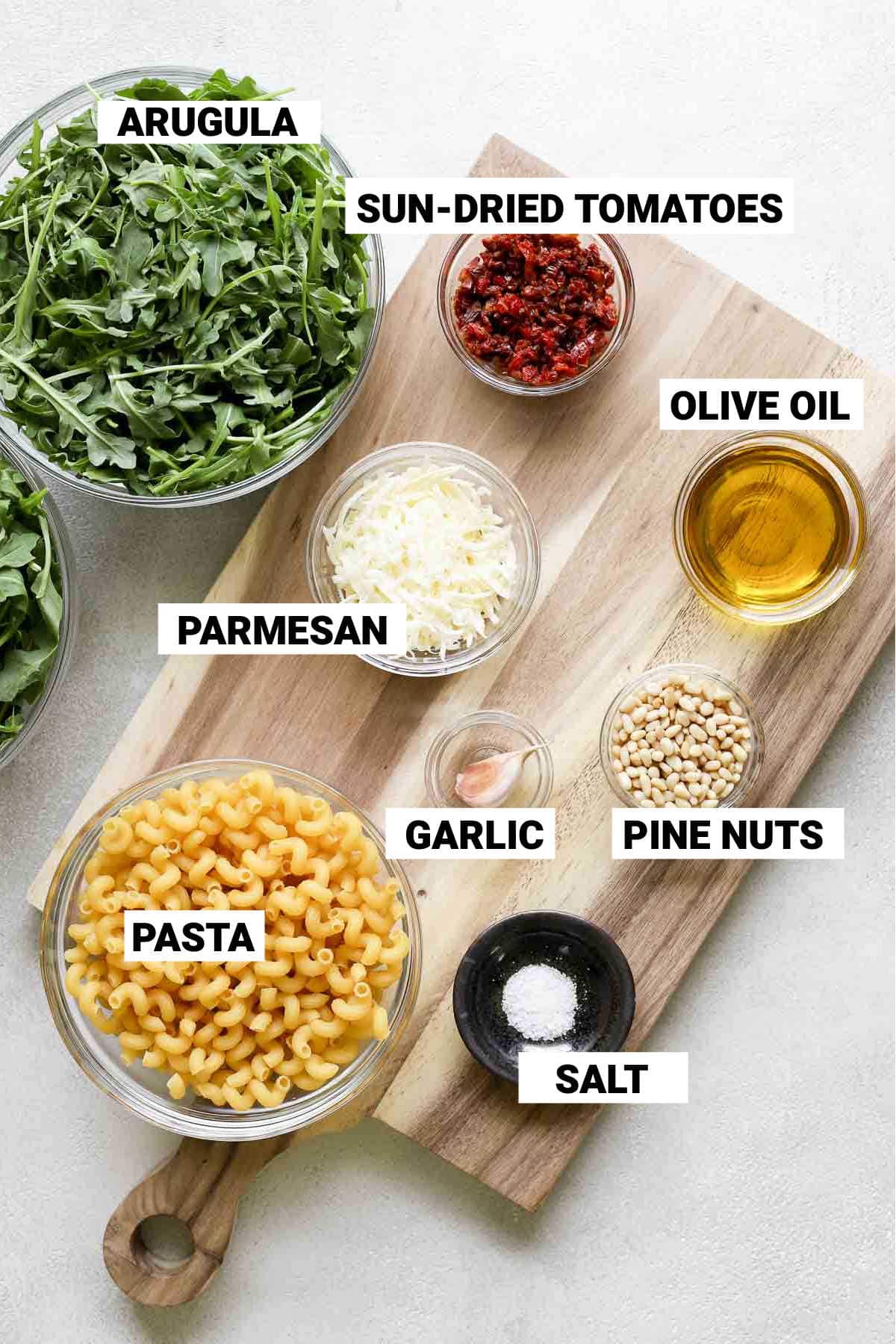 overhead view of arugula pasta ingredients on wooden cutting board with text overlay