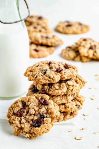 healthy oatmeal cookies stacked on top of each other in the foreground, scattered around in the background, with a jug of milk to the left