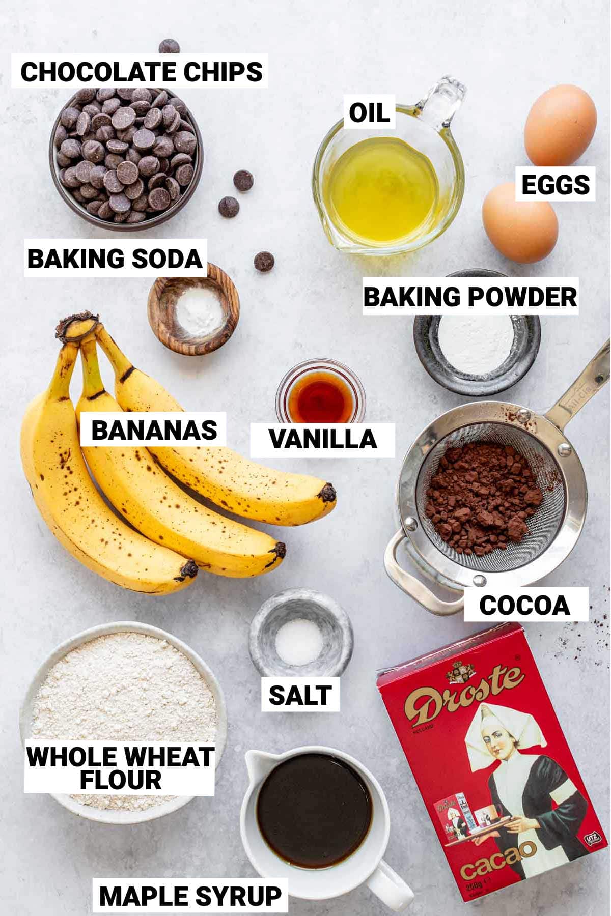 c،colate chips, oil, eggs, baking soda, baking powder, vanilla, banana, salt, cocoa, maple syrup, and w،le wheat flour set out to make w،le wheat c،colate banana bread
