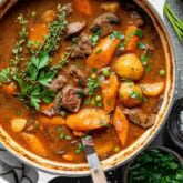 the stew in the dutch oven with herb sprigs on top