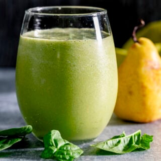 the green smoothie in a tumbler with a yellow pear in the background