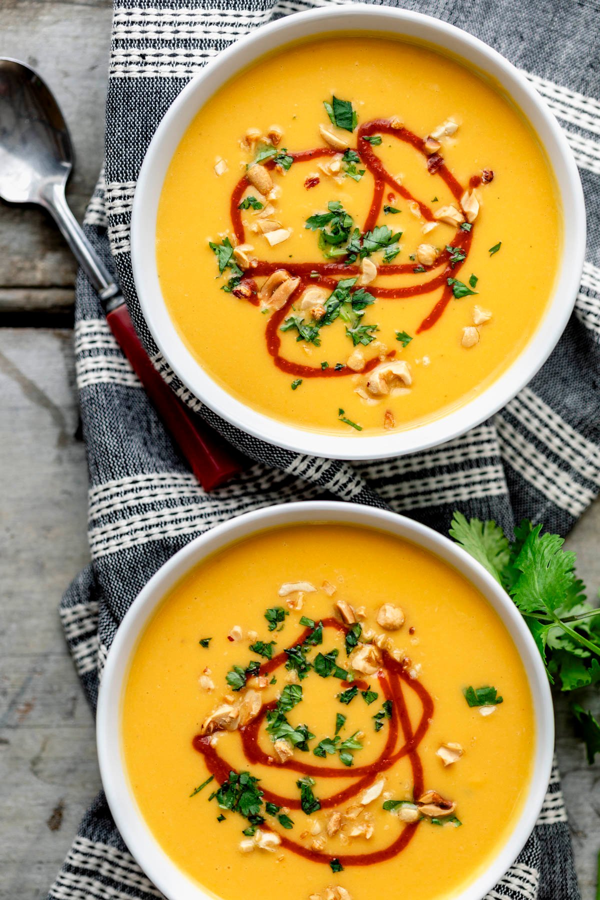 two bowls of sweet potato soup with swirls of hot sauce, chopped peanuts and cilantro on top